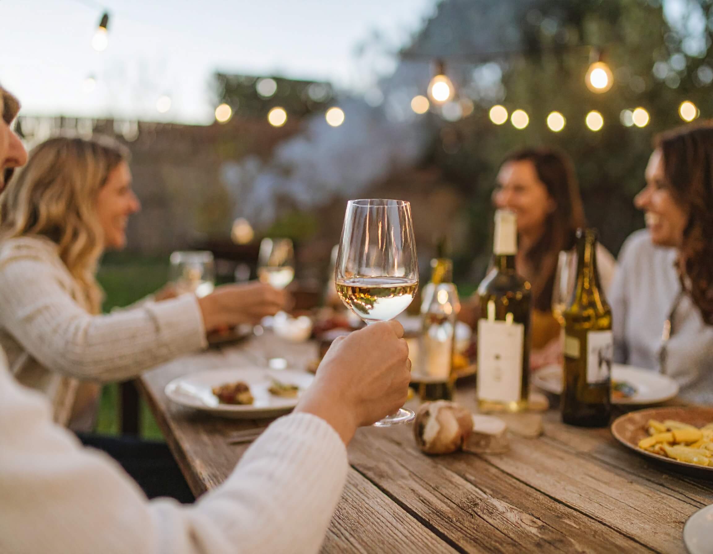 Amigos reunidos alrededor de una mesa tomando vino blanco